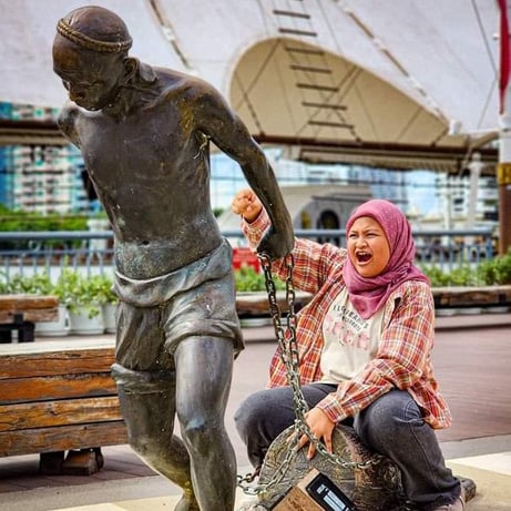 Bangkok, Thailand - a girl sitting on a bench next to a statue of a man at Asiatique Riverfront