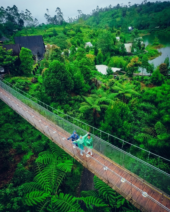 Bandung, Indonesia - a family of three walking across a suspension bridge in the middle of a lush green forest at Resto Bahtera, Glamping Lakeside Rancabali