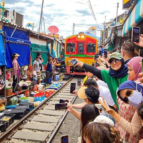 Bangkok, Thailand - a crowd of people taking pictures of a train on the tracks, at Mae Klong railway market (Maeklong)