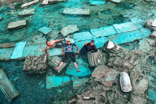 Pamukkale, Turkiye - three people laying in the water at the bottom of Cleopatra's antique pool